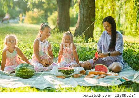 A family in the park, a mother and her children eating watermelon. A healthy lifestyle. A family in the park, a mother and her children eating watermelon. A healthy lifestyle. 125893284