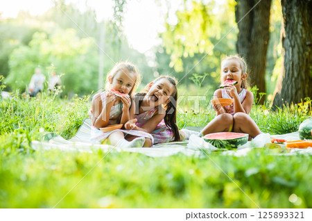 The concept of family and love. Pretty children in summer clothes enjoying a sweet watermelon in the open air. 125893321