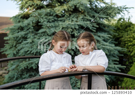 The twin girls look like mirror images of each other. Neat pigtails and white blouses complete the image. The twin girls look like mirror images of each other. Neat pigtails and white blouses complete the image. 125893410