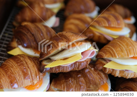 Croissant with egg, jamon blue, cheese Mediterranean appetizer. Breakfast concept. Tasty breakfast with croissant sandwiches with poached egg, avocado, soft cheese, mozzarella and tomato in a plate  125894030
