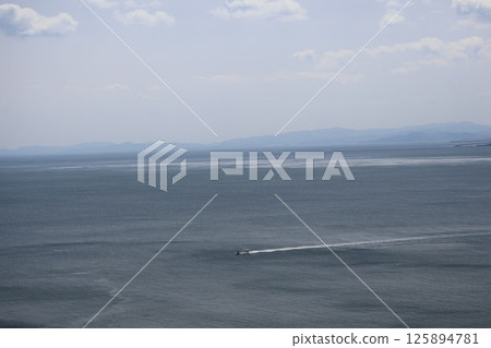 A landscape of blue ocean, boats, hazy mountains, clouds and blue sky 125894781