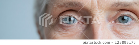 A close-up of an elderly face highlights the beauty of aging, showcasing smooth skin, striking eyes, and abstract lighting in a minimalist style. The composition invites reflection and appreciation 125895173