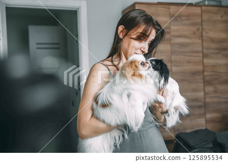 woman tenderly holding two japanese chin dogs, showcasing affection and pet care at home 125895534