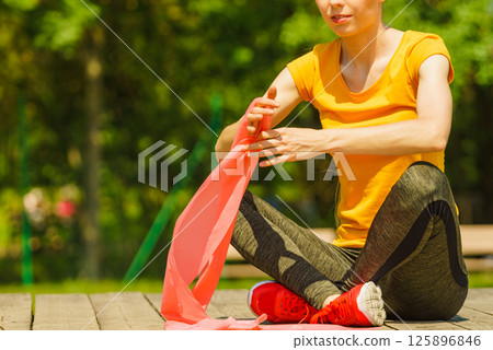 Girl doing exercise outdoor, using resistance fit band. 125896846
