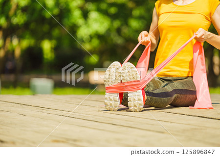Girl doing exercise outdoor, using resistance fit band. 125896847