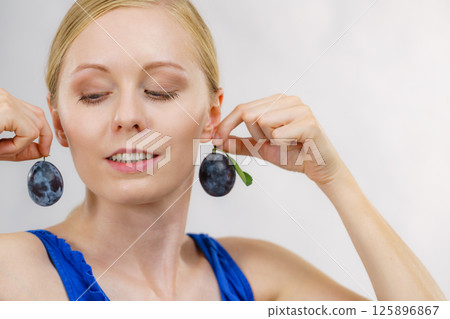 Girl holds plum fruit to her ear 125896867