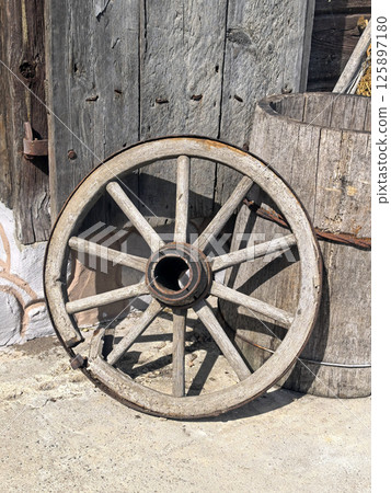An old wooden cart wheel on the background of a wooden bucket and a door. Antique, vintage items. Old transport An old wooden cart wheel on the background of a wooden bucket and a door. Antique, vintage items. Old transport 125897180