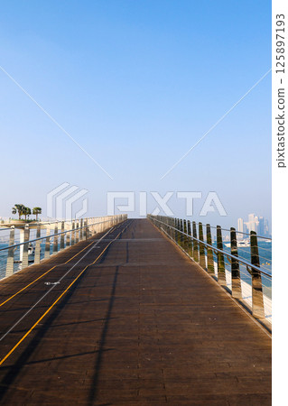 Wooden road into the distance against the backdrop of the sea and tall buildings Wooden road into the distance against the backdrop of the sea and tall buildings 125897193