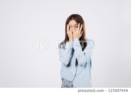 Woman hides in fear, afraid woman covers her face using both hands, reacting to something scary with expressive eyes, on a clean white studio isolated background. Woman hides in fear, afraid woman covers her face using both hands, reacting to something scary with expressive eyes, on a clean white studio isolated background. 125897449