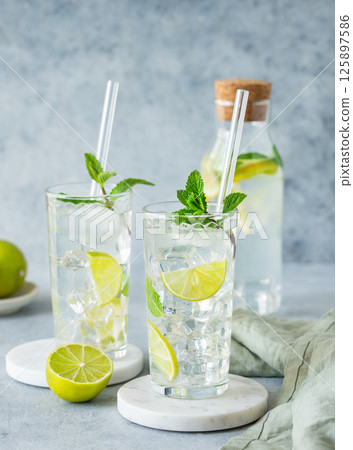 Two glasses and bottle mojito cocktail with fresh lime, mint and ice on a marble stand  125897586