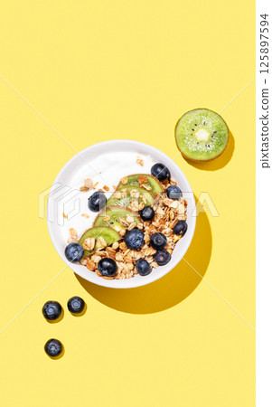 Natural yogurt with granola, kiwi and blueberries in a bowl on a bright yellow background Natural yogurt with granola, kiwi and blueberries in a bowl on a bright yellow background 125897594