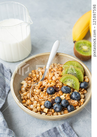Homemade baked granola or muesli in a bowl with kiwi and blueberries on a light background 125897598