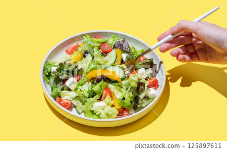 Hand holding fork vegetable salad with lettuce, olives and feta cheese on yellow background. Hand holding fork vegetable salad with lettuce, olives and feta cheese on yellow background. 125897611