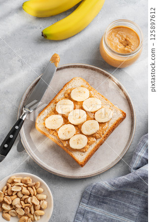 Peanut butter and banana toast on a plate on a light background with morning shadow. 125897612
