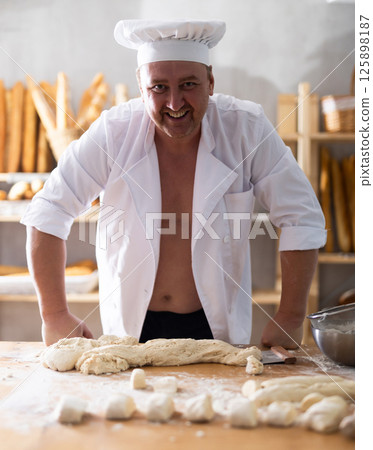 Male baker stands with shirt unbuttoned. Male baker stands with shirt unbuttoned. 125898187