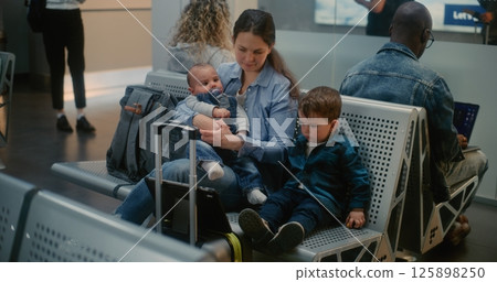 Airport Terminal: Adult Woman with Two Little Kids Sitting and Watching Cartoons on Digital Tablet 125898250