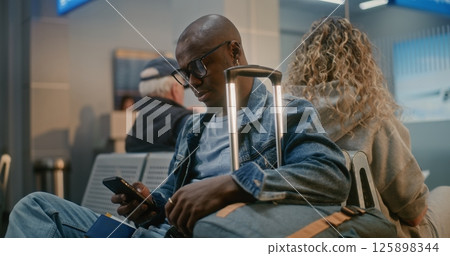 International Airport Terminal: Man with Luggage Sitting, Waiting for Airplane Flight 125898344