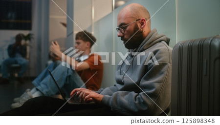 Man Working Online on Laptop, Sending Emails, Sitting on the Floor in Departure Lounge of Airline Hub Man Working Online on Laptop, Sending Emails, Sitting on the Floor in Departure Lounge of Airline Hub 125898348