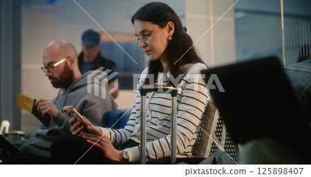 Crowded Airport Terminal: Woman Using Smartphone, Scrolling or Doing Remote Work, Waiting for Flight Crowded Airport Terminal: Woman Using Smartphone, Scrolling or Doing Remote Work, Waiting for Flight 125898407