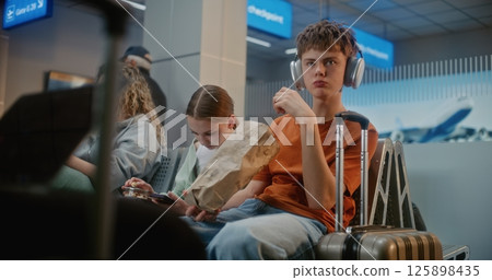Teenage Siblings Eating Snacks, Using Smartphone, Waiting for Flight in Departure Lounge Teenage Siblings Eating Snacks, Using Smartphone, Waiting for Flight in Departure Lounge 125898435