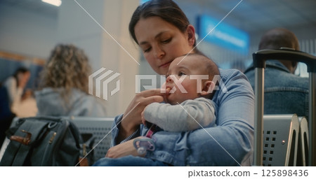 Airport Terminal: Adult Woman Sitting and Feeding Infant While Waiting for Airplane Flight Airport Terminal: Adult Woman Sitting and Feeding Infant While Waiting for Airplane Flight 125898436