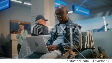 Man Using Laptop, Doing Remote Work, Waiting for Flight in Boarding Lounge of Airline Hub Man Using Laptop, Doing Remote Work, Waiting for Flight in Boarding Lounge of Airline Hub 125898447
