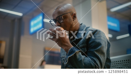 Man Eating Burger and Using Smartphone Sitting in Boarding Lounge of Airport Terminal Man Eating Burger and Using Smartphone Sitting in Boarding Lounge of Airport Terminal 125898451