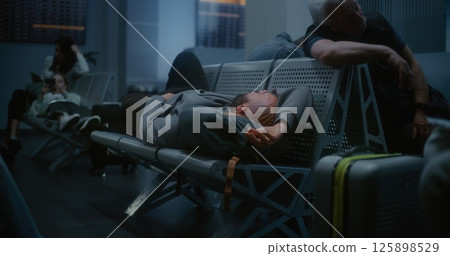 Tired Man Sleeping on Backpack on the Seats in Departure Lounge of Airline Hub at Night Tired Man Sleeping on Backpack on the Seats in Departure Lounge of Airline Hub at Night 125898529