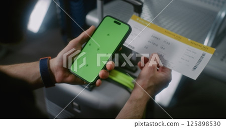 Airport Terminal: Man Sitting in Airline Hub Lounge, Scanning Plane Ticket Using Phone with Green Display Airport Terminal: Man Sitting in Airline Hub Lounge, Scanning Plane Ticket Using Phone with Green Display 125898530