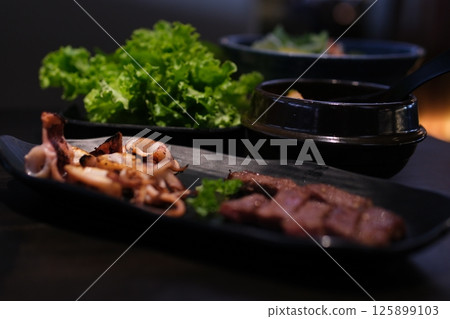 grilled squid pieces meat platter Close-up photo of mixed grilled meat platter. Beef, pork, poultry, sausages, grilled garlic, chili pepper, red tomatoes on wooden rustic background. 125899103