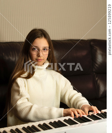 Girl in white sweater playing piano, looking at camera. Girl in white sweater playing piano, looking at camera. 125899219