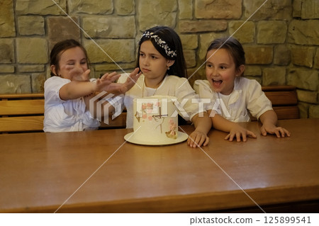 Three girls look at the decorated cake with sparkles in their eyes. Three girls look at the decorated cake with sparkles in their eyes. 125899541