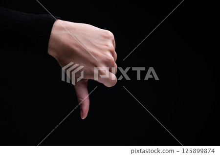 Female hand gesture Thumbs down, on black background. Hand shows gesture of denial or refusal 125899874