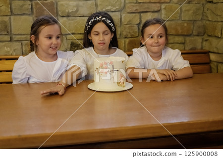 There is a brightly colored cake on the table, and smiling little girls next to it. 125900008