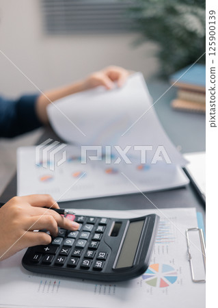 Finance bank tax expense accounting budget money businessman hand use calculator Financial calculate accountant close up calculator with graph chart write office desk Business expense analysis saving 125900139
