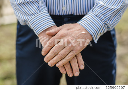 The worn hands of the pensioner are folded. The rough palms of an elderly man. 125900207