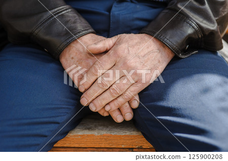 The man's aged hands, firmly folded. The man's trembling fingers.  125900208