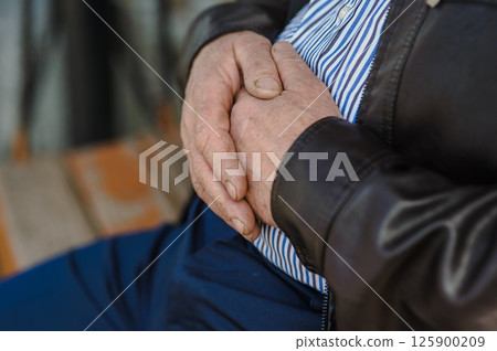 The old man's wrinkled hands are intertwined. The old man's shabby fingers, marked by time. The old man's wrinkled hands are intertwined. The old man's shabby fingers, marked by time. 125900209