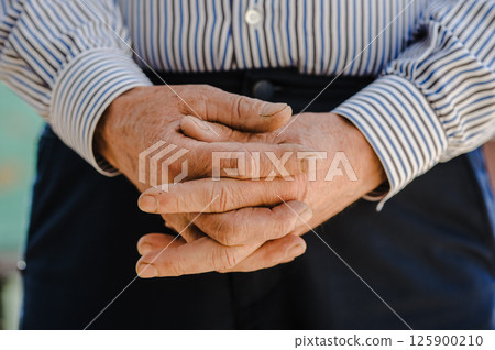 The old man's hands are folded into a lock. His aged fingers tell of past trials. 125900210
