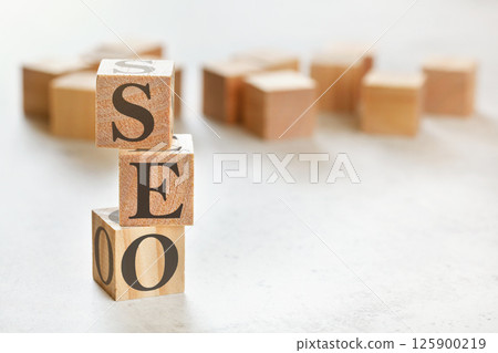 Three wooden cubes with letters SEO (means Search Engine Optimization), on white table, more in background, space for text in right down corner 125900219