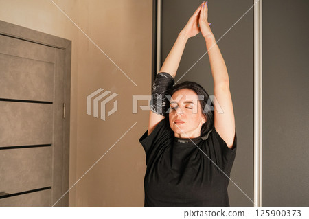 Girl stretches her neck and arms. Daily exercises to maintain posture. Full-body workout at home. Simple and familiar movements are put together in sequential combinations. Girl stretches her neck and arms. Daily exercises to maintain posture. Full-body workout at home. Simple and familiar movements are put together in sequential combinations. 125900373