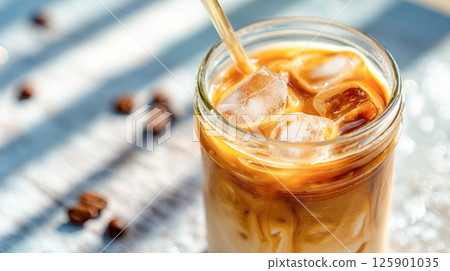 Iced coffee with milk in a glass jar with straw and ice cubes, refreshing summer drink on bright sunny background. 125901035