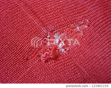 A red wool sweater with a run in it due to a moth hole 125901159