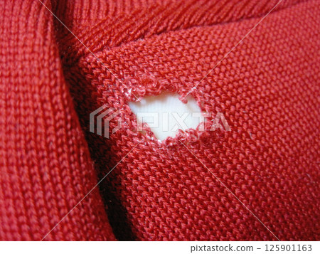 A red wool sweater with a run in it due to a moth hole 125901163