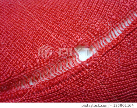 A red wool sweater with a run in it due to a moth hole A red wool sweater with a run in it due to a moth hole 125901164