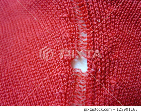 A red wool sweater with a run in it due to a moth hole 125901165