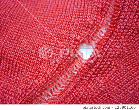 A red wool sweater with a run in it due to a moth hole 125901166