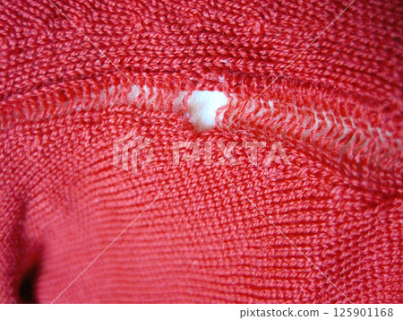 A red wool sweater with a run in it due to a moth hole 125901168
