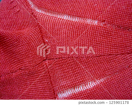 A red wool sweater with a run in it due to a moth hole 125901178