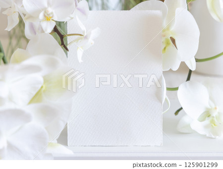 Card near white orchid flowers on table close up, pastel romantic wedding mockup 125901299